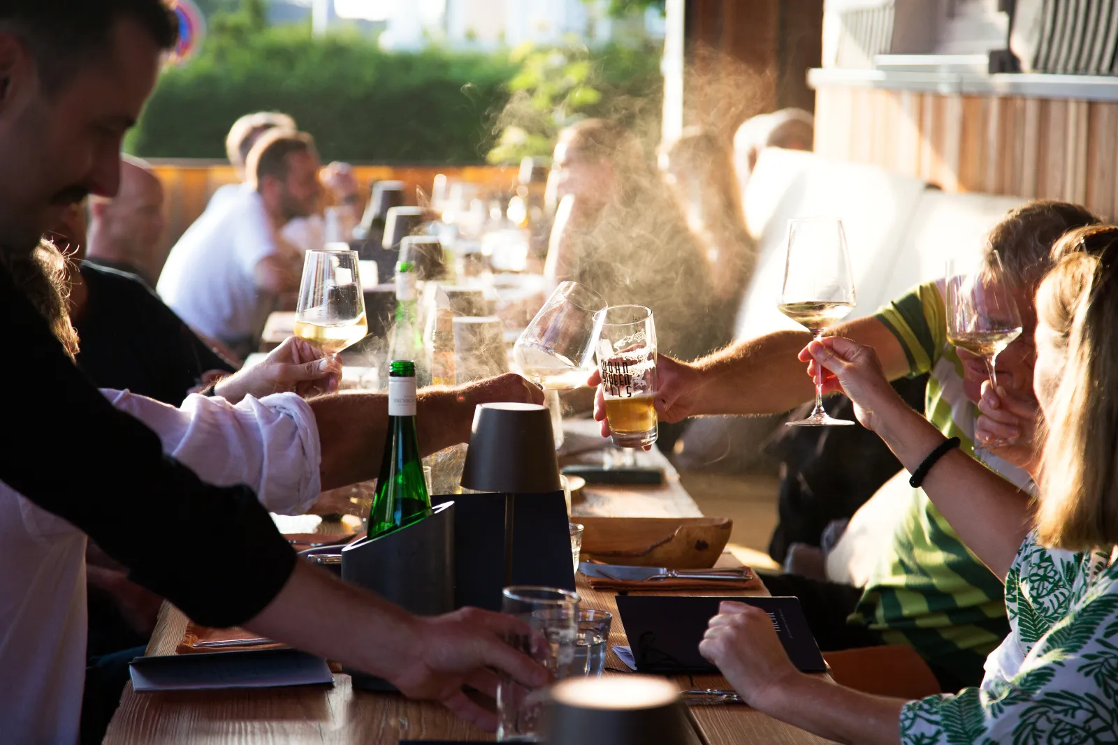 Gäste stoßen bei Abendsonne auf der Terrasse des Vergissmeinnicht mit Wein und Bier an