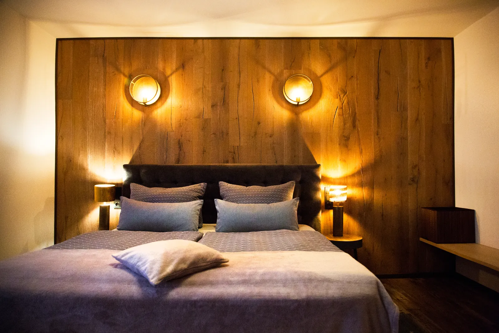 Hotelzimmer mit Eichenholz-Wand, Doppelbett und warmen Messing-Wandleuchten