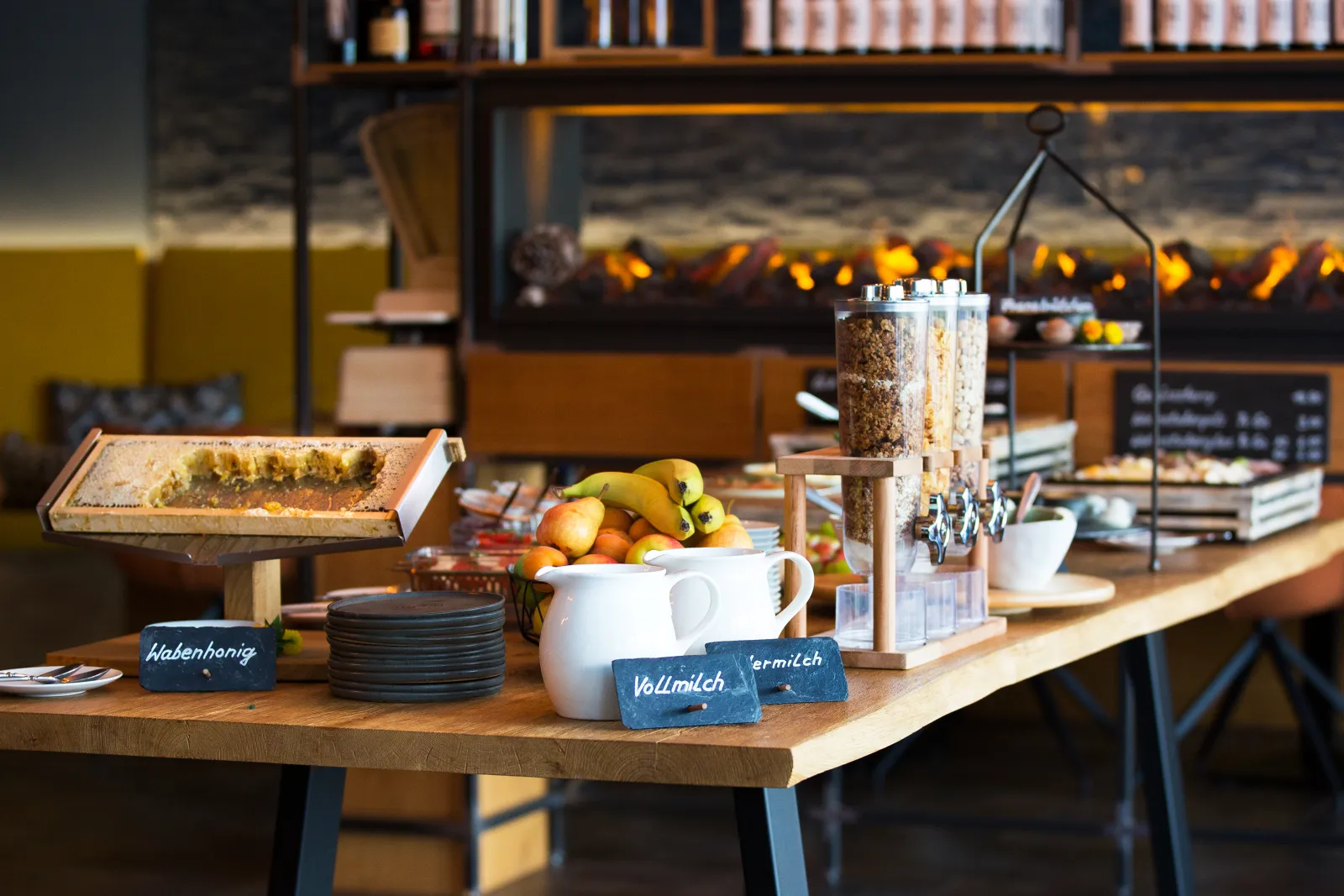 Frühstücksbuffet mit Wabenhonig, frischem Obst und Müsli, Kamin im Hintergrund