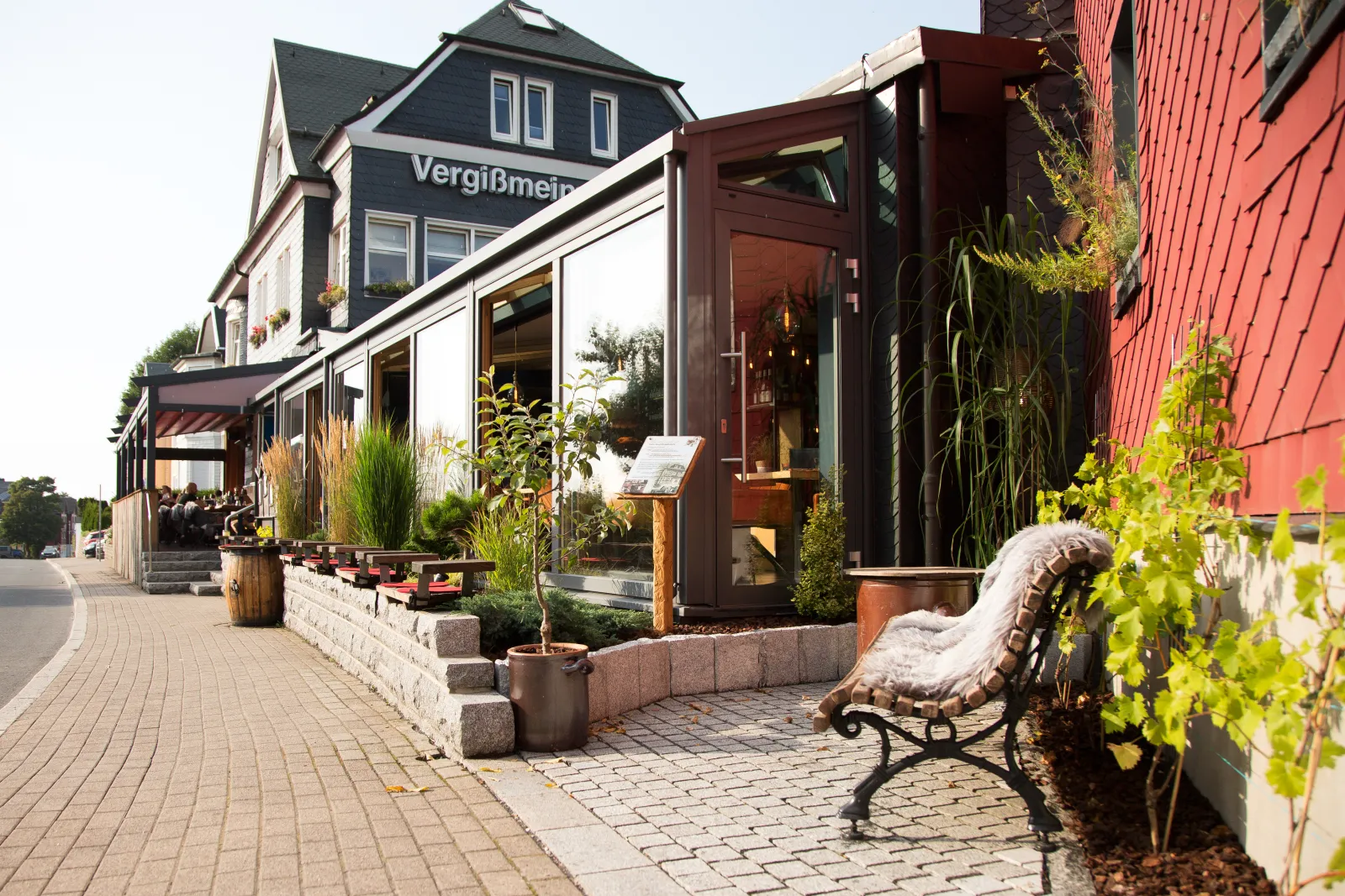 Das Restaurant & Hotel Vergissmeinnicht in Oberhof mit Terrasse, Bänken und Bepflanzung an der Straße