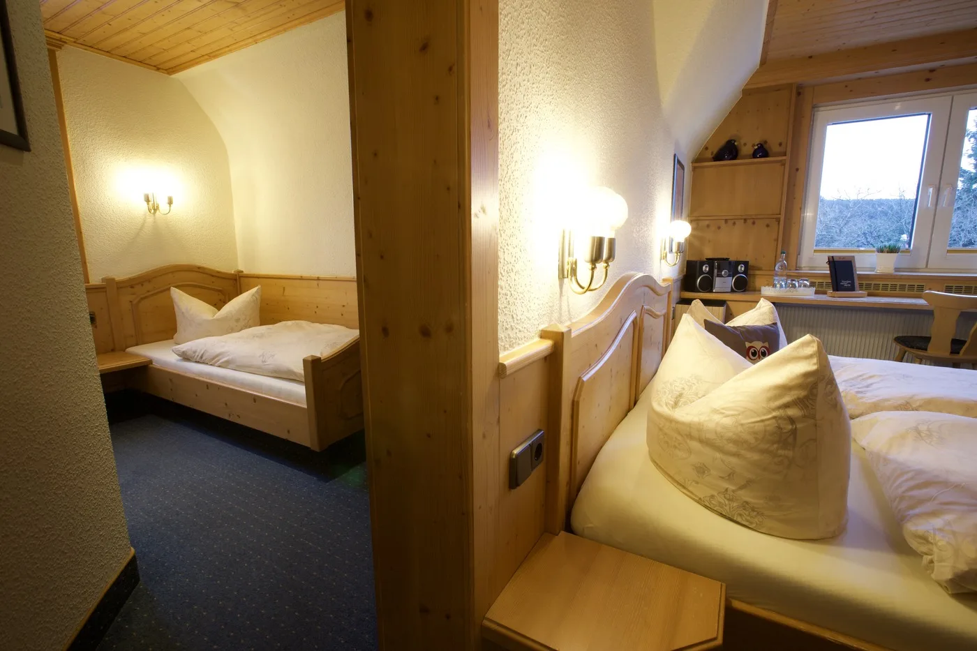 Dreibettzimmer mit Einzel- und Doppelbett, Sitzecke und warmen Wandleuchten