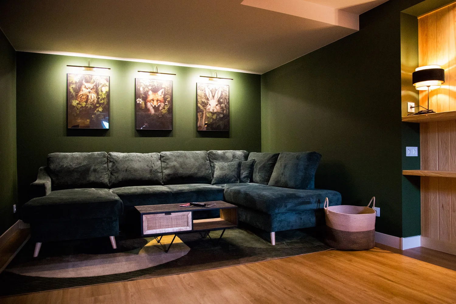 Wohnzimmer im Ferienhaus Vergissmeinnicht mit grünem Ecksofa, Bildern an der Wand und warmem Licht